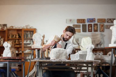 Sakallı zanaatkar bir keskiyle beyaz taş oymacılığında çalışıyor. Sanat eserleri ile yaratıcı atölye.