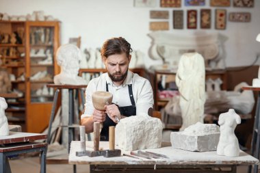 Beyaz gömlekli ve siyah önlüklü erkek heykeltıraş sanat stüdyosunda kadın gövdesinin kireçtaşından bir kopyasını yapıyor..