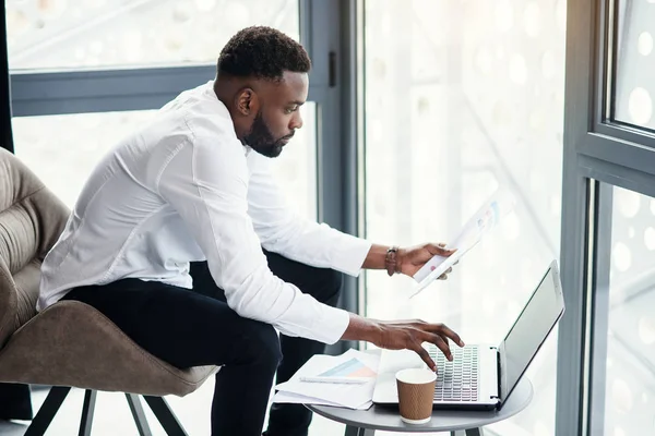 Hombre de negocios afroamericano guapo que trabaja en la computadora portátil y el análisis en la habitación especialmente designada en la oficina moderna y elegante . — Foto de Stock