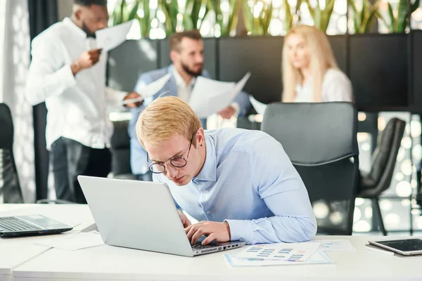 带着滑稽眼镜的快乐而有目的的男性办公室职员坐在他的工作场所，用笔记本电脑解决经济问题. — 图库照片