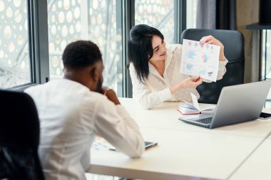 Sempatik iş ortakları toplantı odasındaki toplantı masasında haritalarla finansal belgeleri dikkatle inceliyor..