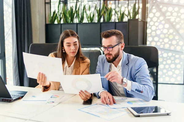 Likable purposeful business partners carefully studying financial documents with charts at the boardroom table at the meeting room. — Stock Photo, Image