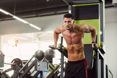 Modern spor salonunda antrenman yaparken güçlü ve sağlıklı bir adam paralel barlarda şınav çekiyor. Sportif ve sağlıklı bir kavram. Dolly vurdu..