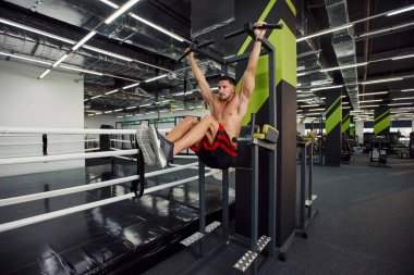 Çapraz çubukta, siyah ve yeşil iç mekanı olan modern bir spor salonunda karın egzersizi yapan güçlü bir adam..