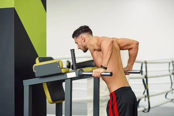 Hombre de fitness deportivo haciendo flexiones en barras paralelas durante el entrenamiento en el gimnasio moderno. Concepto saludable y deportivo . — Foto de Stock