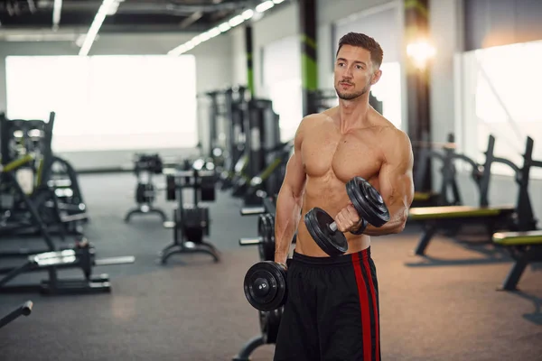 Healthy man doing biceps exercises with dumbbells on the training in modern gym. — ストック写真