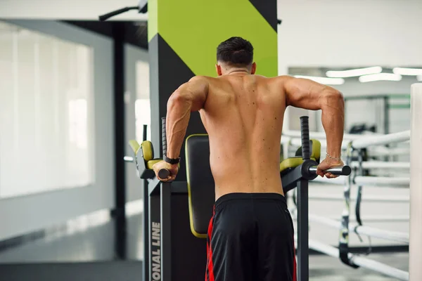 Hombre fuerte haciendo flexiones en barras paralelas durante el entrenamiento en el gimnasio moderno. Vista trasera. Concepto deportivo y saludable . — Foto de Stock