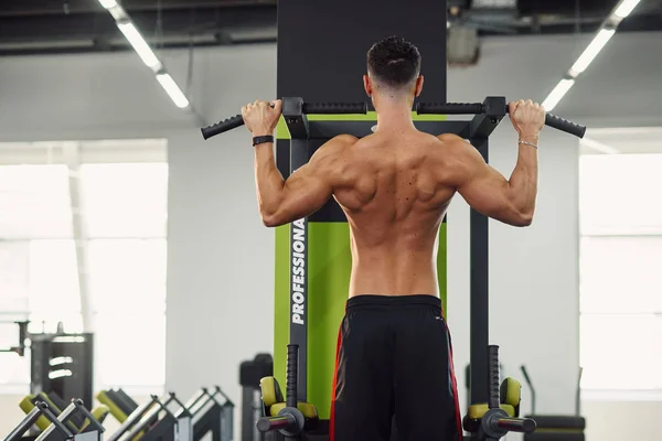 Strong man does pull-up on the crossbar during training in the modern gym. Back view. — Stock Photo, Image