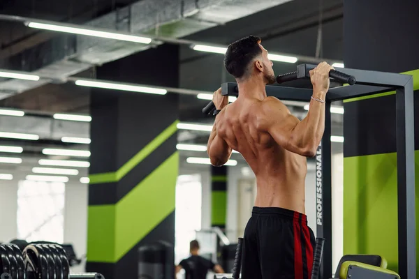 Hombre fuerte hace pull-up en el travesaño durante el entrenamiento en el gimnasio moderno. Vista trasera . — Foto de Stock