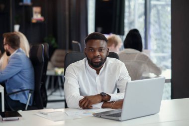 Memnuniyet duyan Afro-Amerikan ofis müdürü laptopun başında gülümsüyor ve başparmağını kaldırıyor..