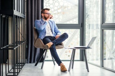 Başarılı iş adamı dinleniyor ve modern ofis odasında güzel kokulu kahve içiyor. Başarılı genç iş adamı.