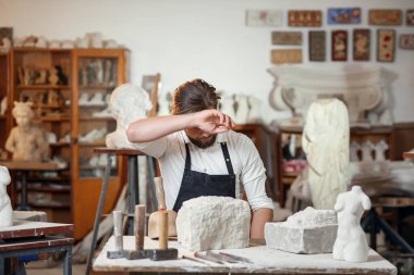 Beyaz gömlekli ve siyah önlüklü erkek heykeltıraş sanat stüdyosunda kadın gövdesinin kireçtaşından bir kopyasını yapıyor..