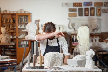 Beyaz gömlekli ve siyah önlüklü erkek heykeltıraş sanat stüdyosunda kadın gövdesinin kireçtaşından bir kopyasını yapıyor..
