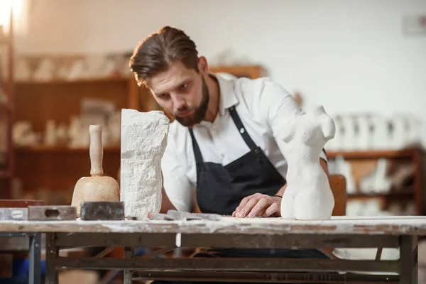 Bearded sculptor measures stone woman torso to make copy of it from limestone at creative studio.