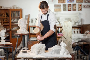 Sakallı zanaatkar bir keskiyle beyaz taş oymacılığında çalışıyor. Sanat eserleri ile yaratıcı atölye.