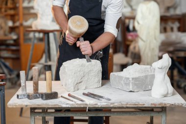 Sakallı zanaatkar bir keskiyle beyaz taş oymacılığında çalışıyor. Sanat eserleri ile yaratıcı atölye.