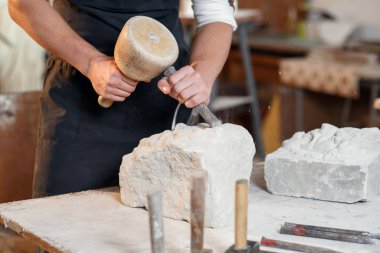 Sakallı zanaatkar bir keskiyle beyaz taş oymacılığında çalışıyor. Sanat eserleri ile yaratıcı atölye.