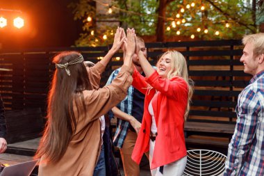Group of young caucasian friends giving high five together and celebrating party in house courtyard at the evening.
