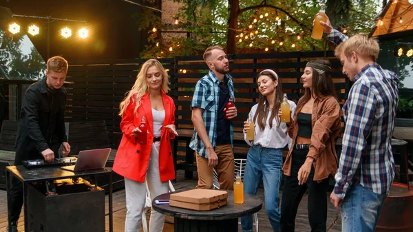 Grupo de jovens amigos alegres estão desfrutando de um tempo juntos em uma festa de churrasco no acolhedor jardim da noite . — Fotografia de Stock