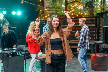 Arkadaşları dışarıda kutlama partisinde renkli lambaların ışığında dans ederken güzel bir kız ön planda dans ediyor..