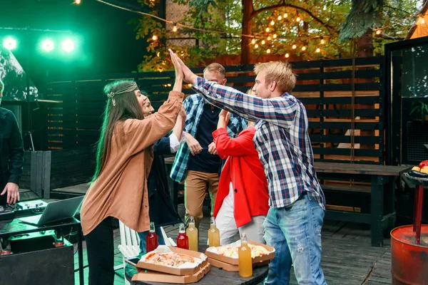 Grupo de jovens amigos caucasianos dando alta cinco juntos e celebrando festa no pátio da casa à noite . — Fotografia de Stock