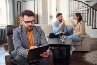 Depresyondaki çift koltukta oturup birbiriyle tartışırken psikolog doktor da notlar alıyor..