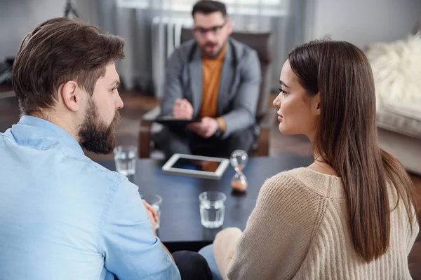 Depressed young couple of man and woman speaking with psychologist on therapy session in modern office. Bad relationships without future. — Stock Photo, Image