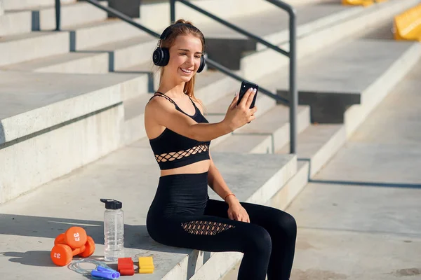 Bild der erstaunlichen jungen Sportlerin, die draußen sitzt, macht ein Selfie mit dem Handy, das Friedensgeste zeigt. — Stockfoto