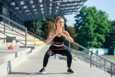 Genç sportif kadın lastik bantla dışarıda egzersiz yapıyor.