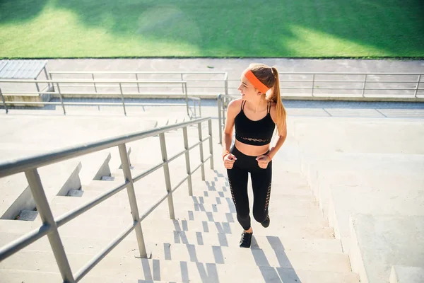 Atleta corriendo por las escaleras de un estadio. Mujer en ropa de fitness haciendo ejercicio corriendo en las escaleras junto a los asientos de un estadio . —  Fotos de Stock