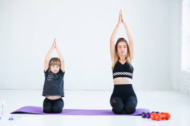 Güzel atletik genç kız ve küçük kız kardeşi beyaz stüdyoda yoga yapıyorlar ve Lotus pozuna konsantre olmuşlar..
