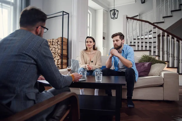 Close up of male psychologist sits at chair and listens depressed young couple at stylish cozy office. Selective focus. — Stock Photo, Image