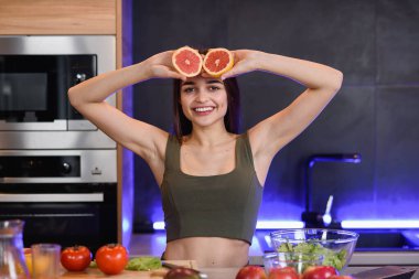 Komik ve neşeli genç kadın gözlerinin yanında portakal dilimleri tutarak ve gülümseyerek.