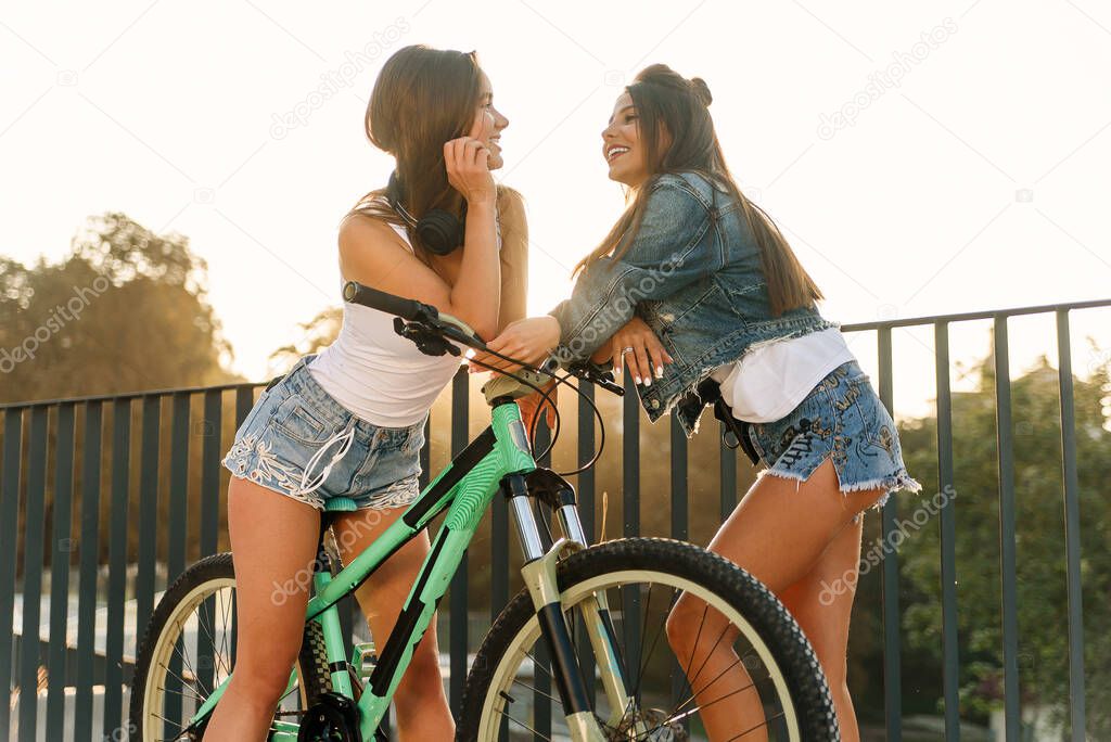 One trendy 30s girl with bike waiting for her hot female friend in tempting shorts on the specially equipped observation deck
