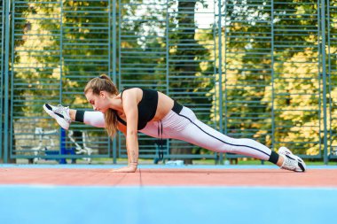 Çekici kız dışarıda bisiklet pistinde sicimin üzerinde oturuyor. Ellerini yere koydu ve kameraya doğru baktı. Kız gri spor giyer ve koyu renk spor ayakkabı giyer. Yatay.