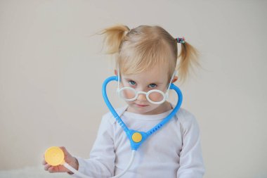 Stetoskop oyuncağıyla doktor ve hastane gibi oynayan neşeli kız evde eğleniyor..