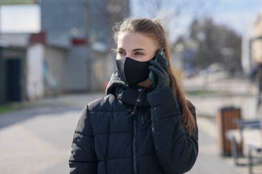 Dışarıda akıllı telefon kullanan koruyucu maskeli ve eldivenli bir kız. COVID 19. Dünya koronavirüs salgını.
