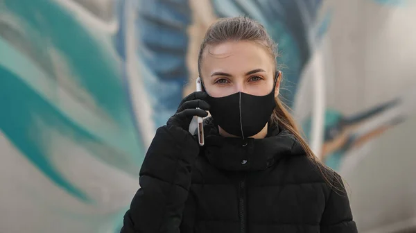 Chica joven en la calle de la ciudad vistiendo máscara médica estéril negro. Mujer usando el teléfono para buscar noticias sobre nCov 2019. Cuarentena COVID-19 epidemia de coronavirus pandémico y concepto de atención sanitaria — Foto de Stock