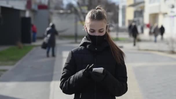 戴着防护面具和手套的女孩在户外使用智能手机。COVID 19.世界大肠癌大流行病. — 图库视频影像