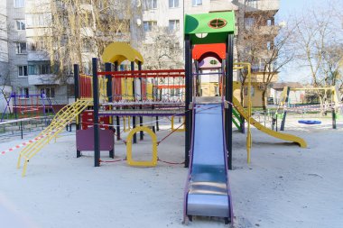 Coronavirus COVID-19 kısıtlaması. Karantina yüzünden kimse yok. Şehirdeki kapalı çocuk oyun parkı. Boş park ve oyun alanı. Evinizde kalabilirsiniz. Salıncak ve slaytlarda kırmızı uyarı bandı