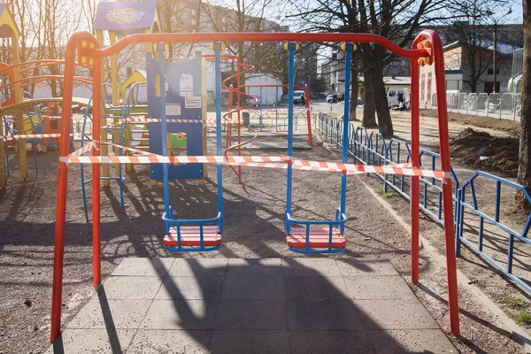 Детская площадка закрыта и завернута в тревожную ленту, предостерегающую от глобального коронавирусного карантина. Детей на игровых площадках нет. Профилактика коронавируса COVID-19 . — стоковое фото