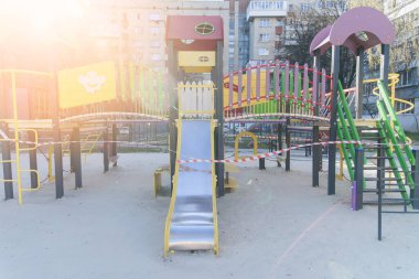 Coronavirus COVID-19 kısıtlaması. Karantina yüzünden kimse yok. Şehirdeki kapalı çocuk oyun parkı. Boş park ve oyun alanı. Evinizde kalabilirsiniz. Salıncak ve slaytlarda kırmızı uyarı bandı