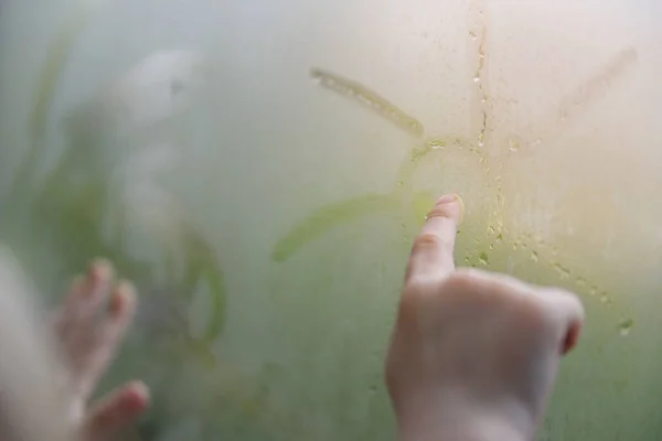 El muchacho en la ventana en un día lluvioso dibuja el sol en la ventana nebulosa —  Fotos de Stock