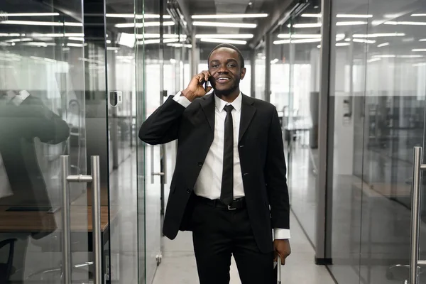 El hombre de negocios exitoso tiene conversación telefónica mientras está parado en el pasillo vacío de la oficina. Banquero profesional masculino de traje hablando por teléfono móvil durante el descanso laboral. — Foto de Stock