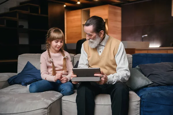 Grandpa with his granddaughter using tablet at cozy home.