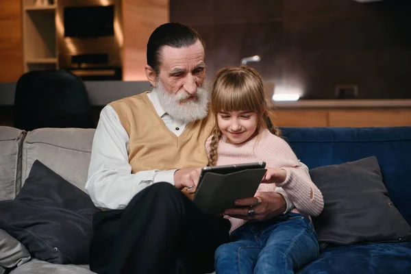 Grandpa with his granddaughter using tablet at cozy home.