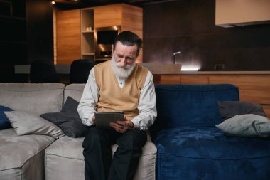 Yaşlı adam tablet bilgisayar öğreniyor. Yaşlılar için elektronik aletler. Şık sakallı bir adam web sörfü için tablet kullanıyor..