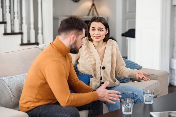 Angry couple having argument or breakup. Young husband and wife having quarrel while sitting on a couch in the living room in a big house. Infidelity concept. — Stock Photo, Image