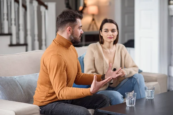 Angry couple having argument or breakup. Young husband and wife having quarrel while sitting on a couch in the living room in a big house. Infidelity concept. — Stock Photo, Image