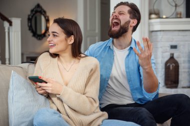 Genç kadın koltukta otururken akıllı telefon kullanıyor ve kocası da arkasından üzülüyor. Akıllı telefon bağımlılığı nedeniyle ailede sorunlar var..